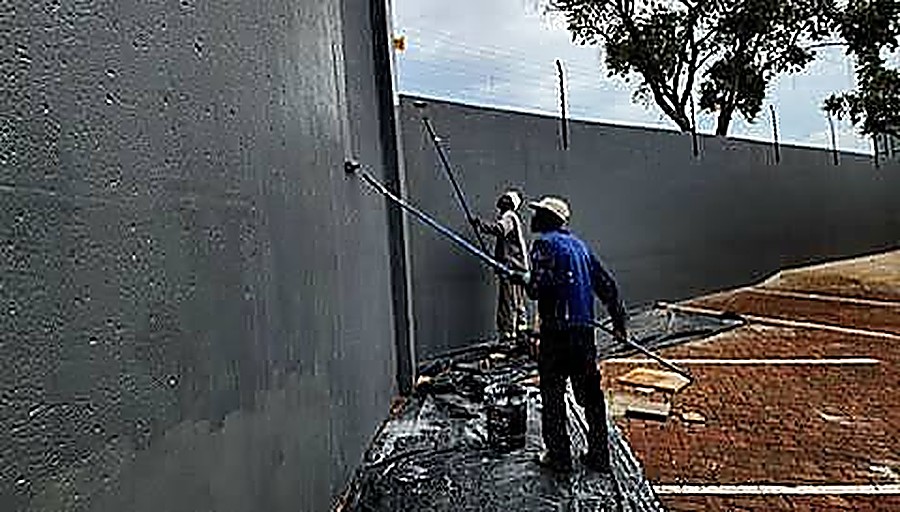 Painters coating a long boundary wall with a roller on an extension pole
