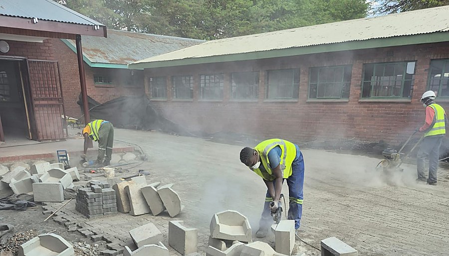 Workers cutting precast paver and edging units on site with a plate compactor in the background