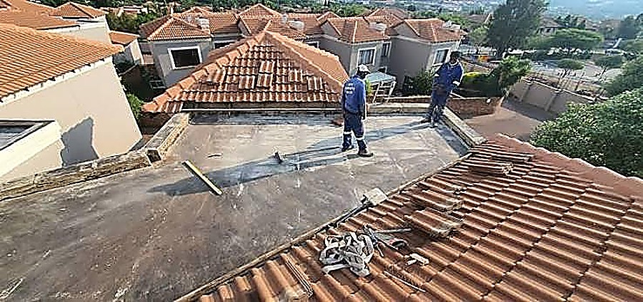 Flat roof waterproofing preparation next to a tiled roof section